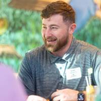 Scott Hilgendorf sitting with pizza and smiling as he chats with others